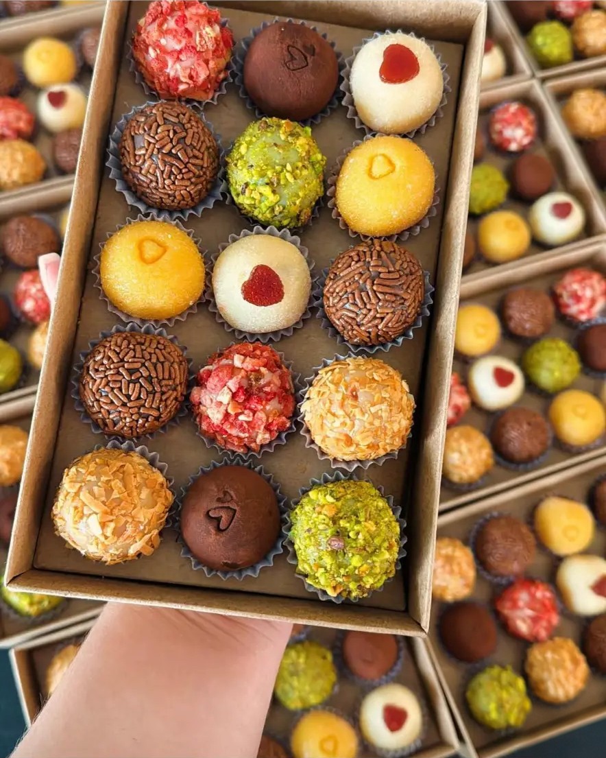 A kraft box filled with assorted brigadeiros, held in hand